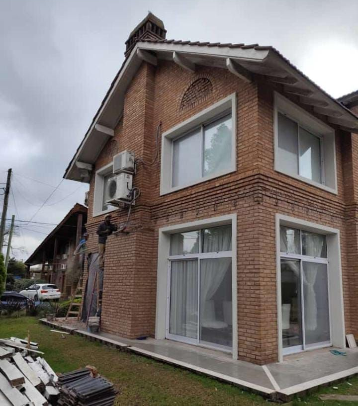 Casa de ladrillo de dos pisos con ventanas de marco blanco y chimenea, en un día nublado