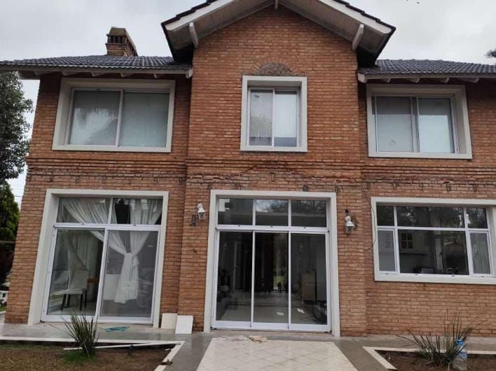 Casa de ladrillo de dos pisos con ventanas de marco blanco y una puerta corrediza de vidrio central.
