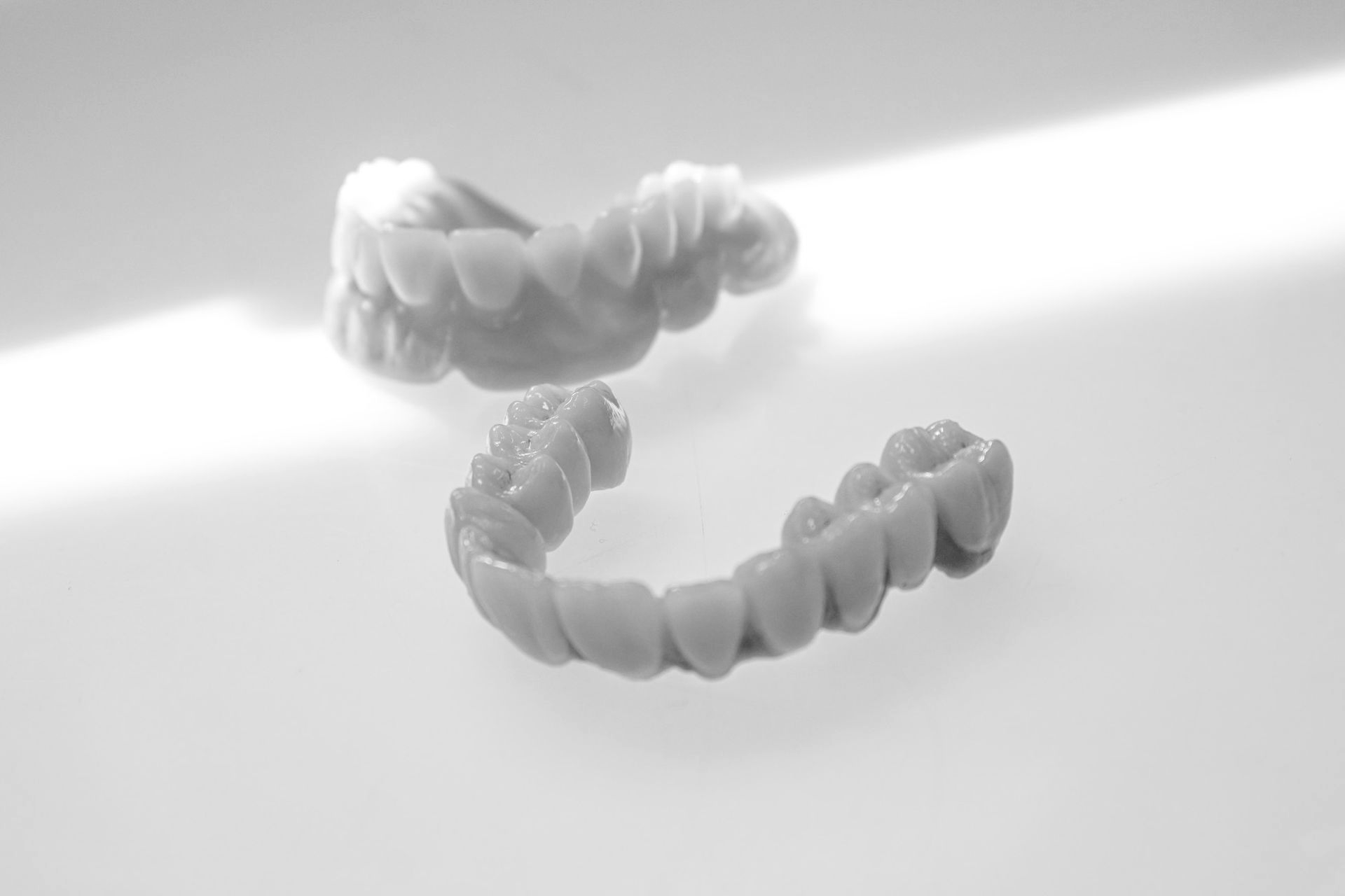 Zwei Zahnprothesen liegen auf einer weißen Oberfläche und werden vom Sonnenlicht beleuchtet.