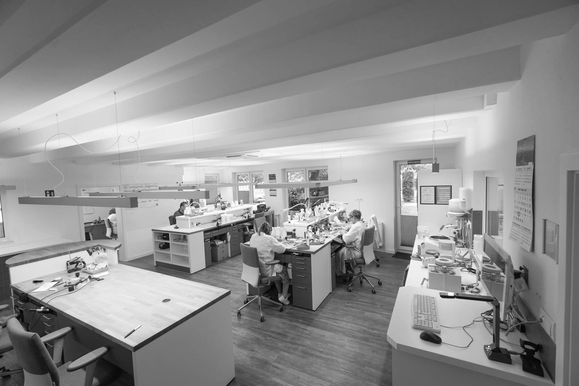 Helles, geräumiges Dentallabor mit mehreren Mitarbeitern an Stationen. 