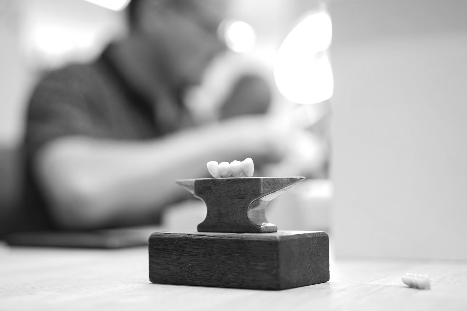 Ein kleiner Zahn auf einem Miniaturamboss, mit einer verschwommenen Person im Hintergrund.