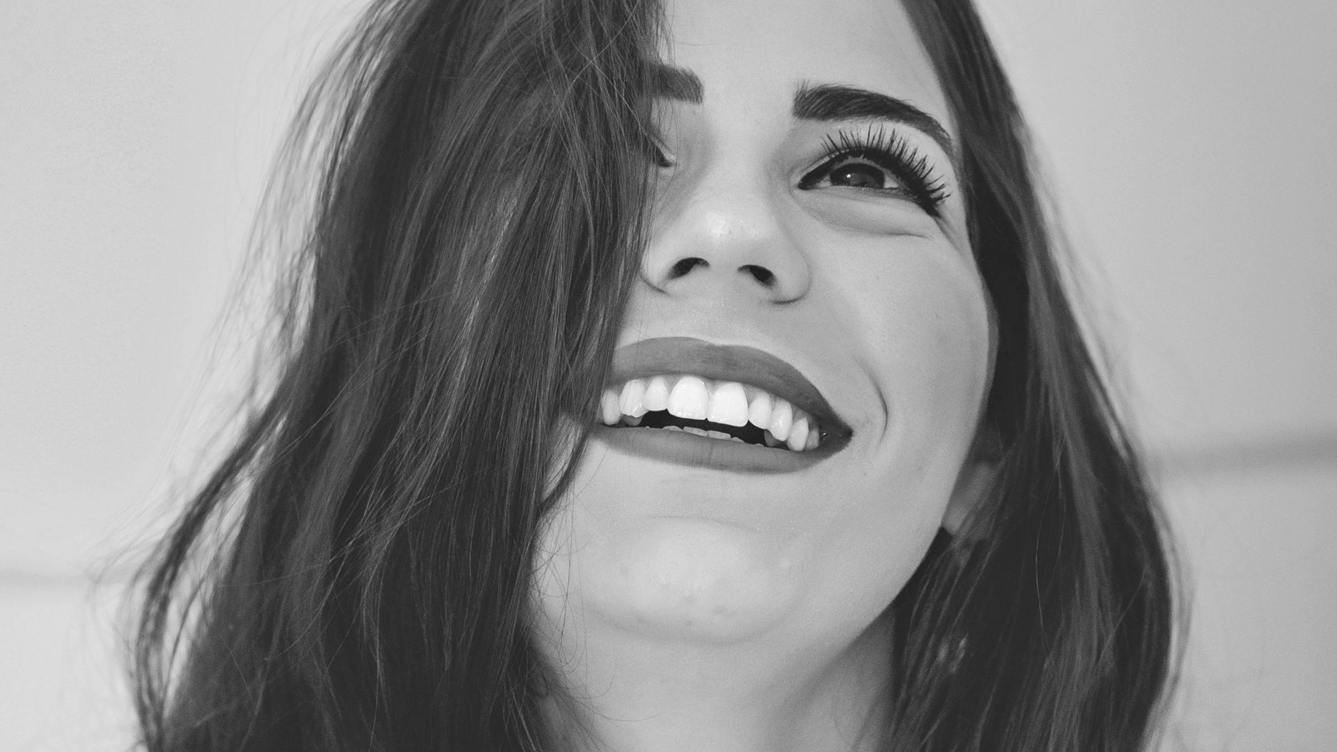 Frau mit braunem Haar lächelt und schaut nach oben; roter Lippenstift.