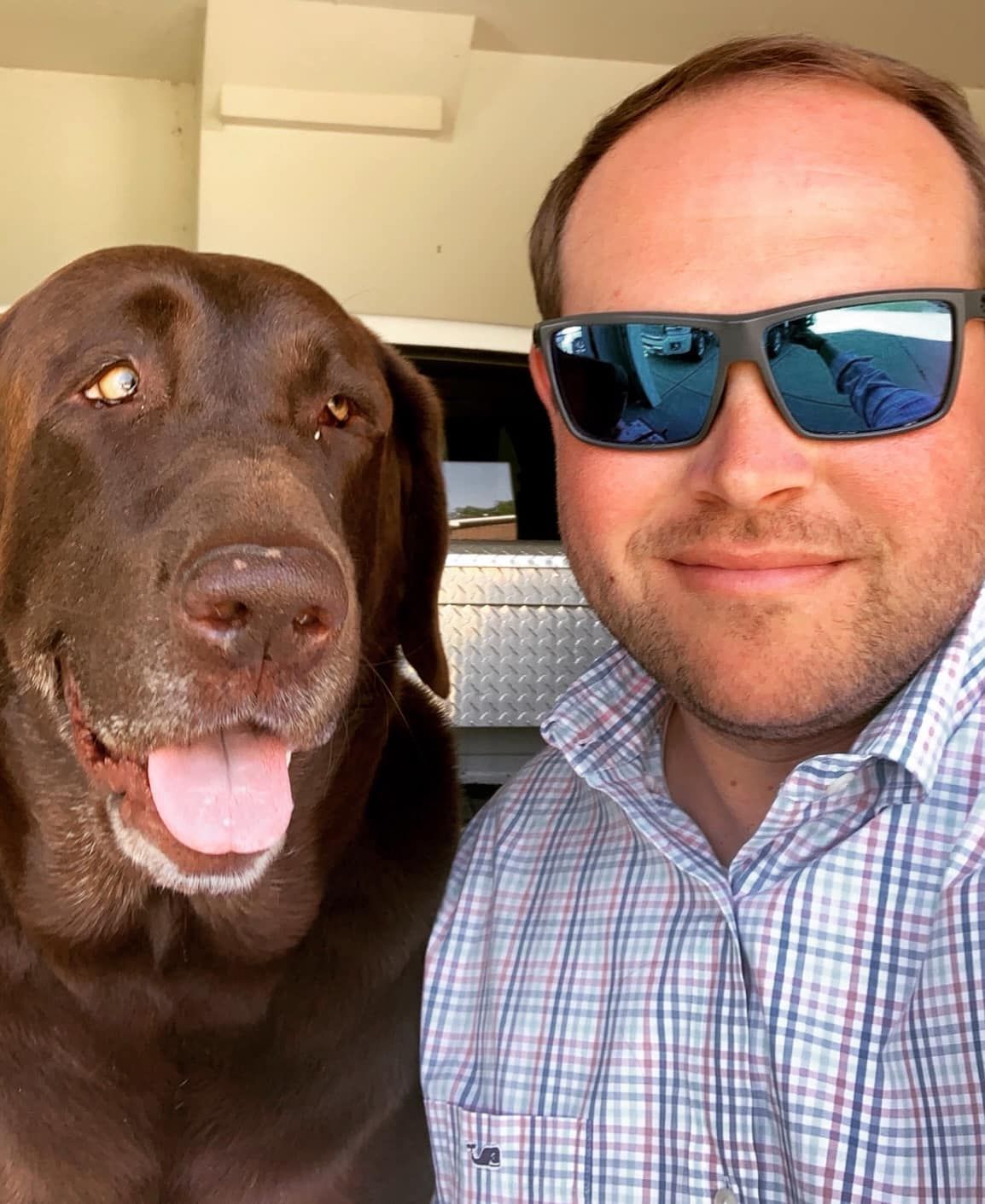 A man wearing sunglasses is standing next to a brown dog.