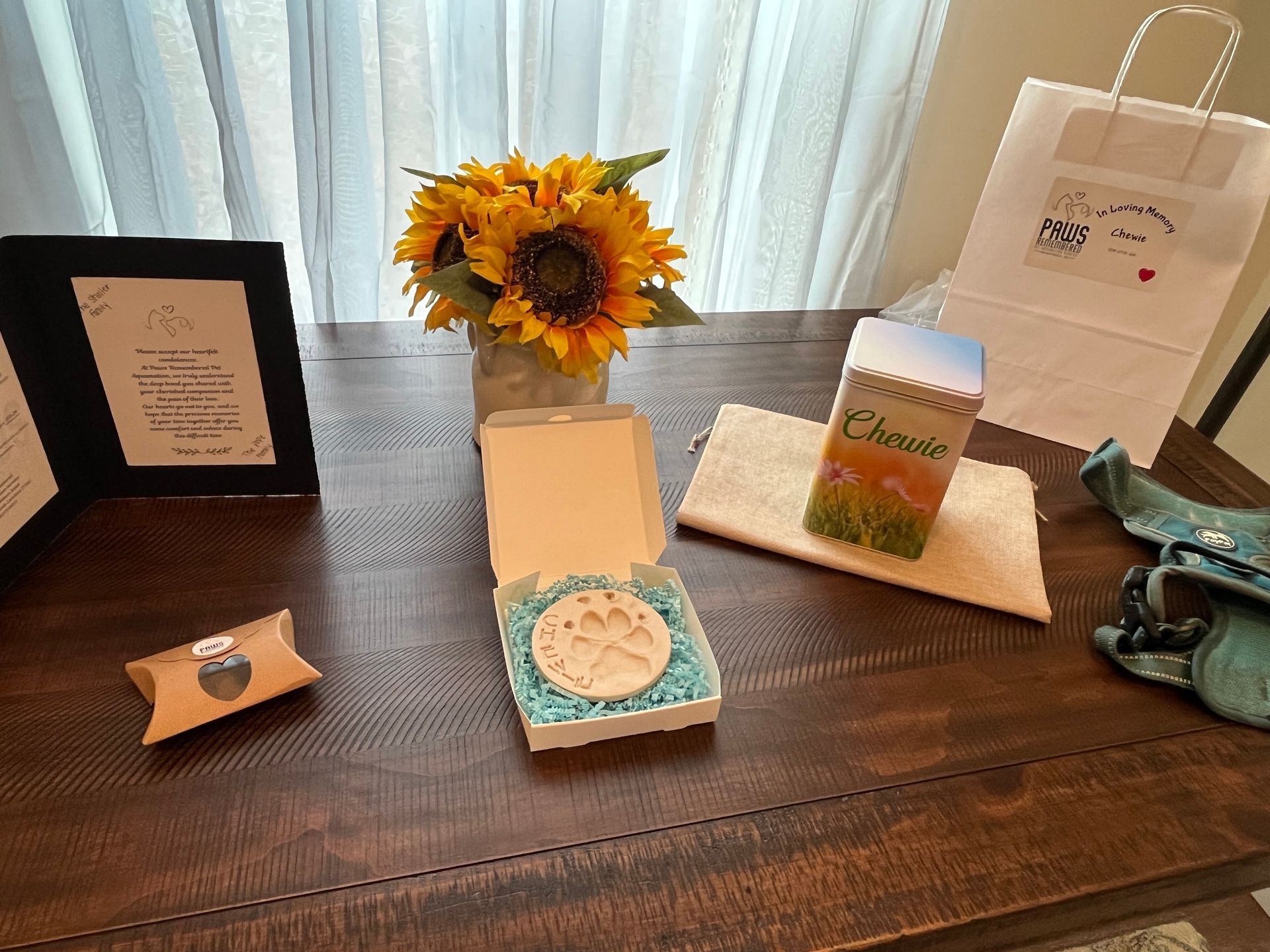 A wooden table topped with a vase of sunflowers , a box , a picture frame , and a bag.