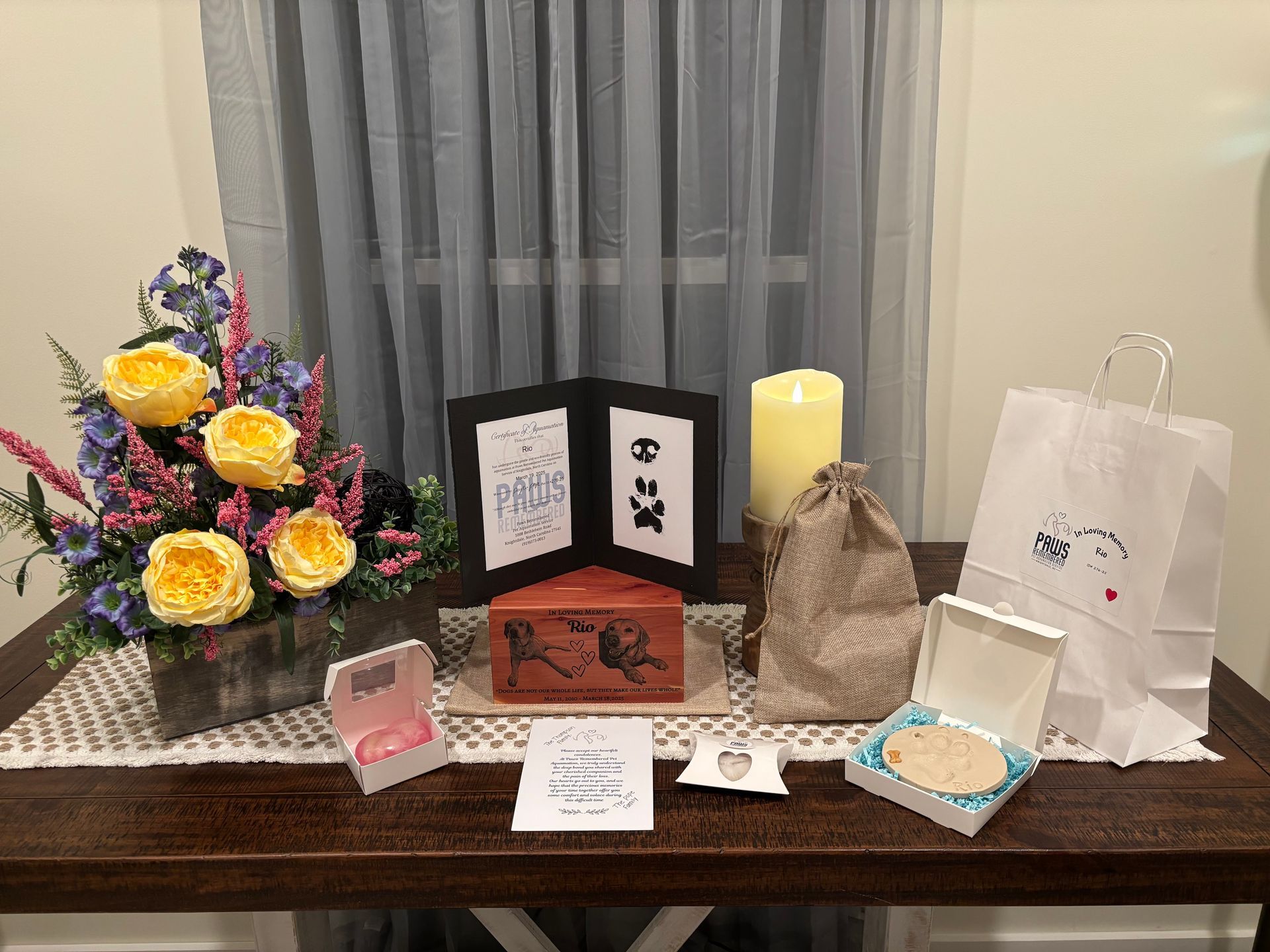 A table with a vase of flowers , candles , boxes , and a bag on it.