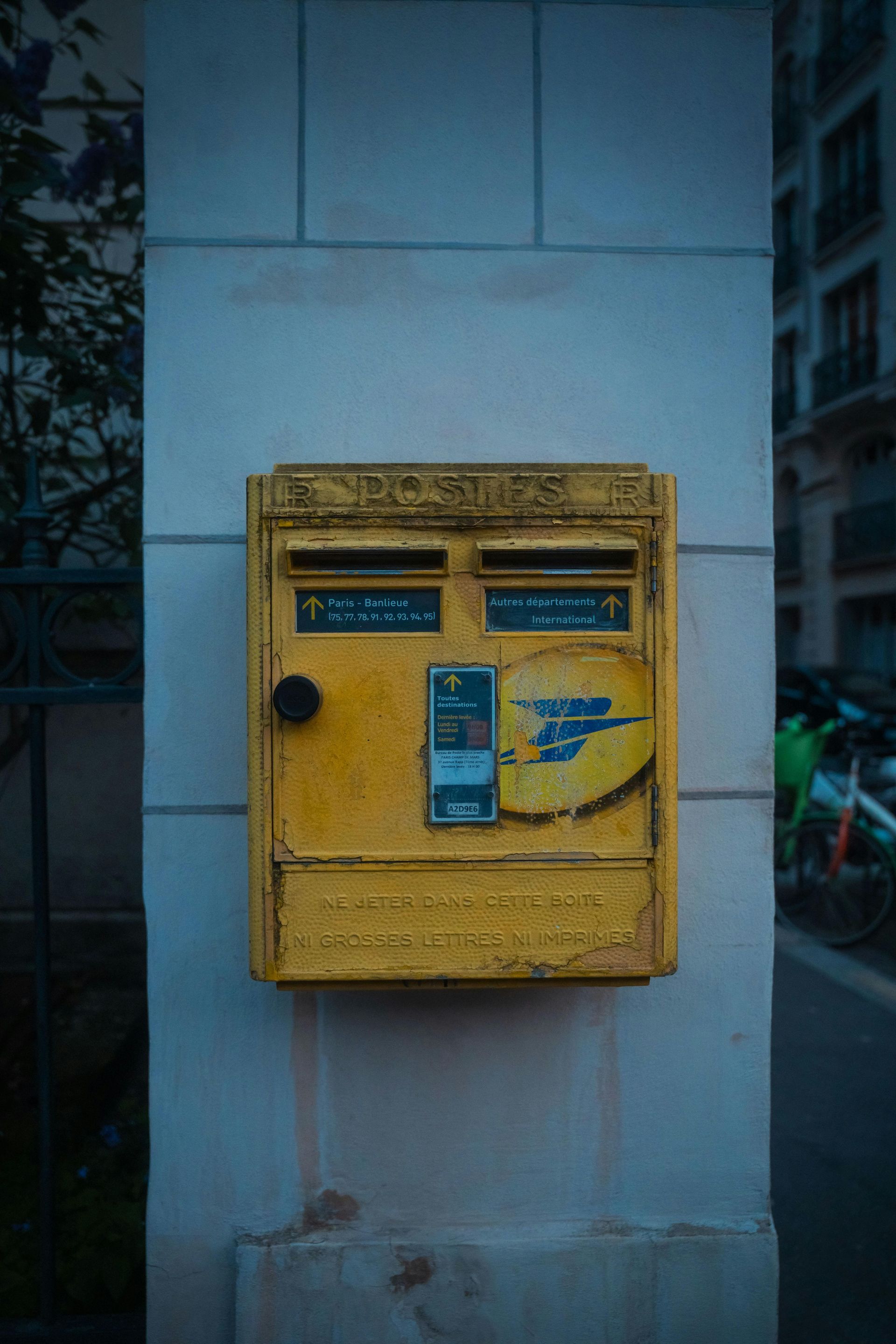 Yellow French mailbox mounted on a stone column.