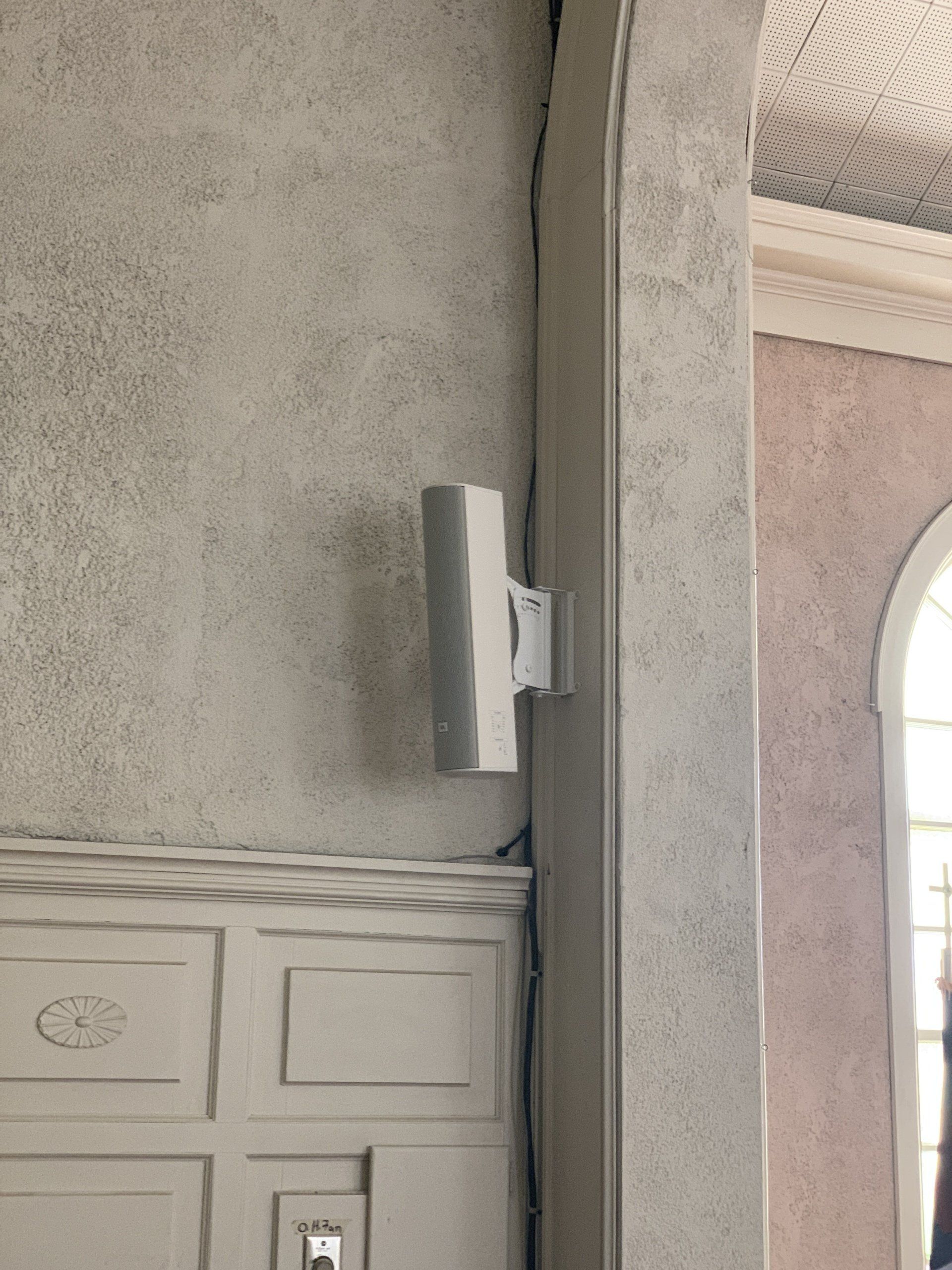 A white speaker is mounted to a wall next to a door