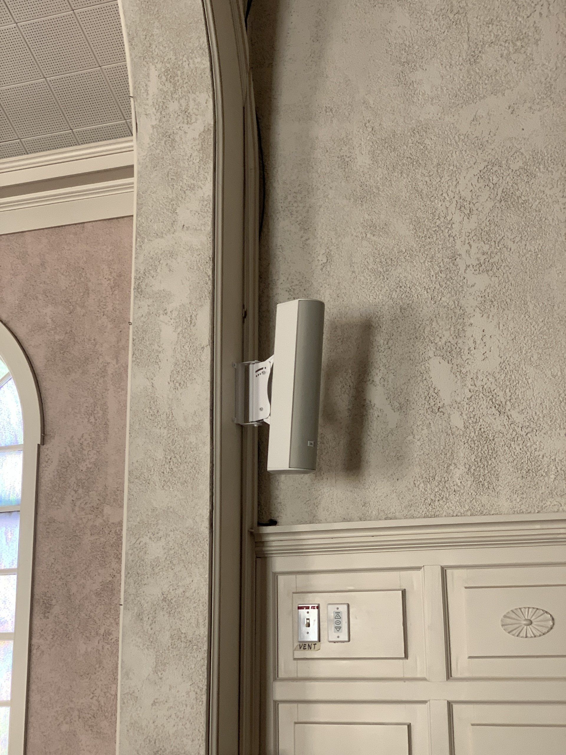 A white speaker is mounted on a wall next to a door.