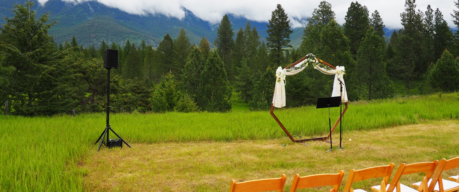 A wedding ceremony is taking place in a field with mountains in the background.