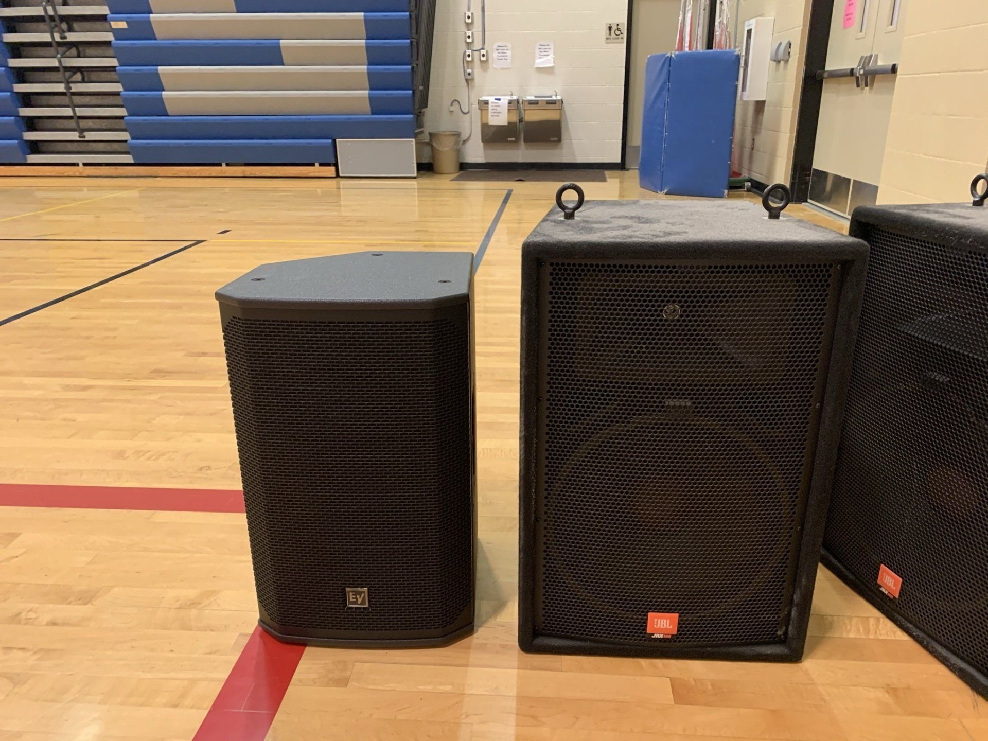 Two speakers are sitting on a wooden floor in a gym.
