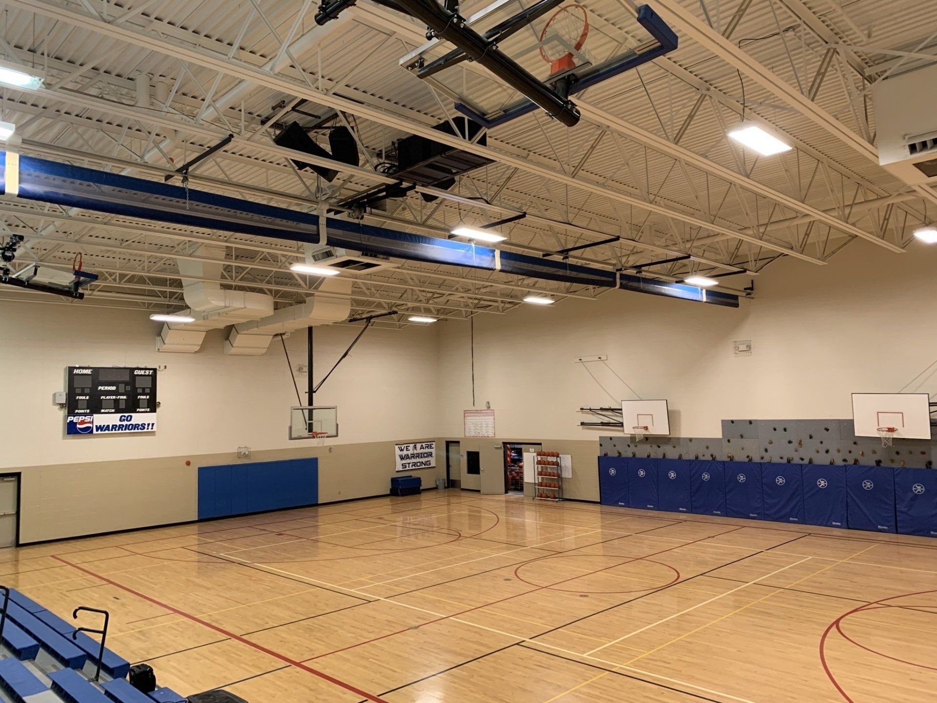 An empty gym with a basketball hoop and a scoreboard.