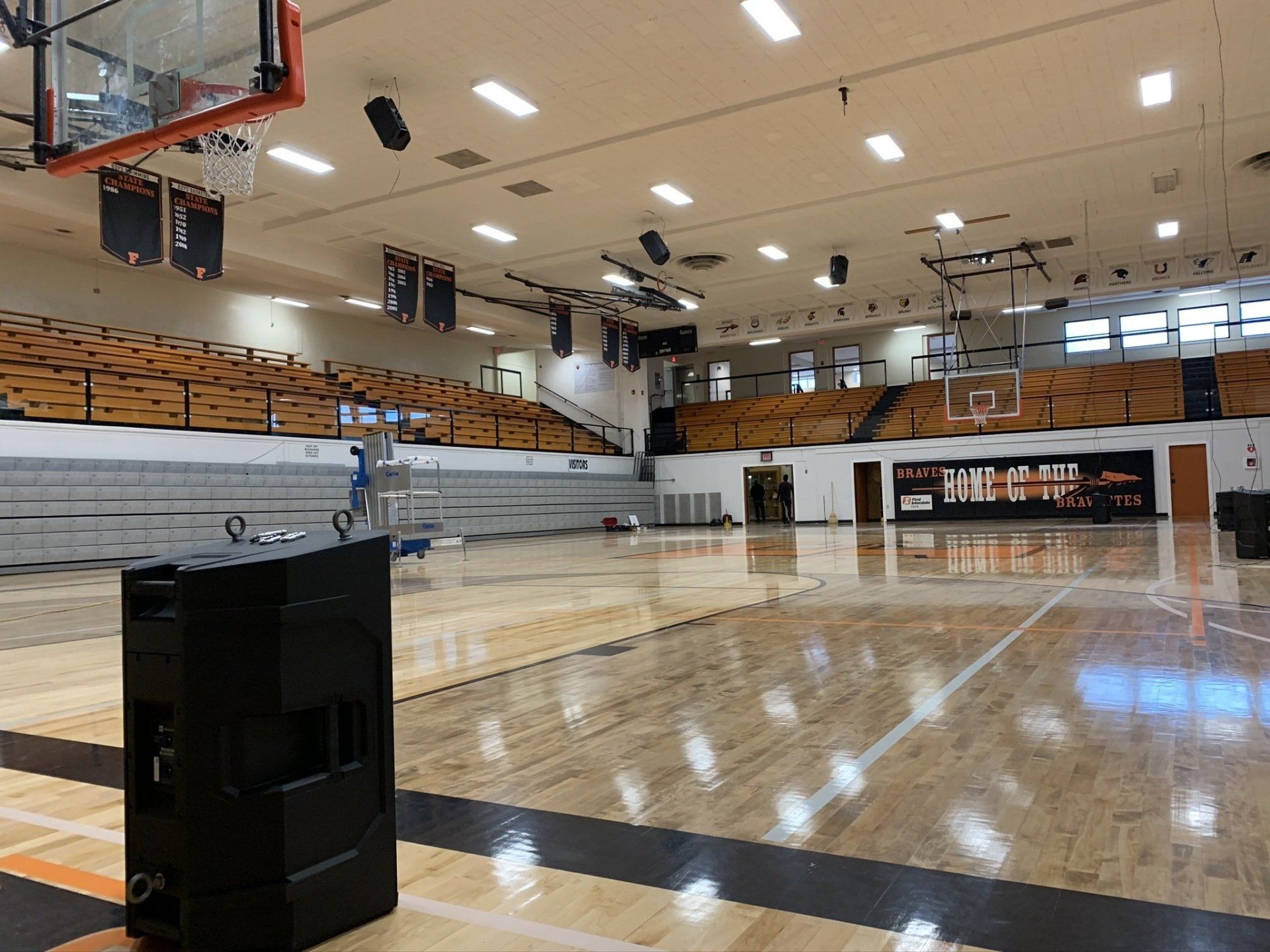 An empty basketball court in a gym with a speaker in the foreground