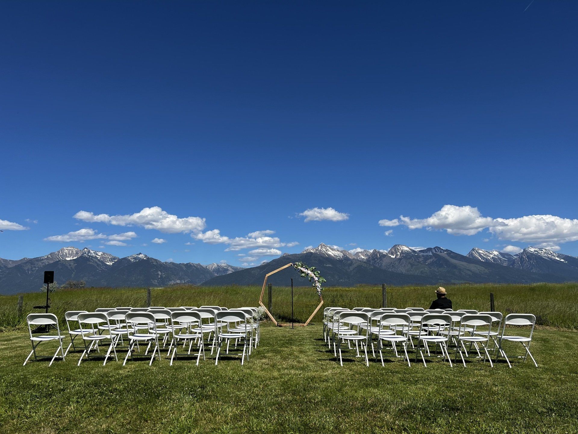 A row of folding chairs are lined up in a field with mountains in the background.