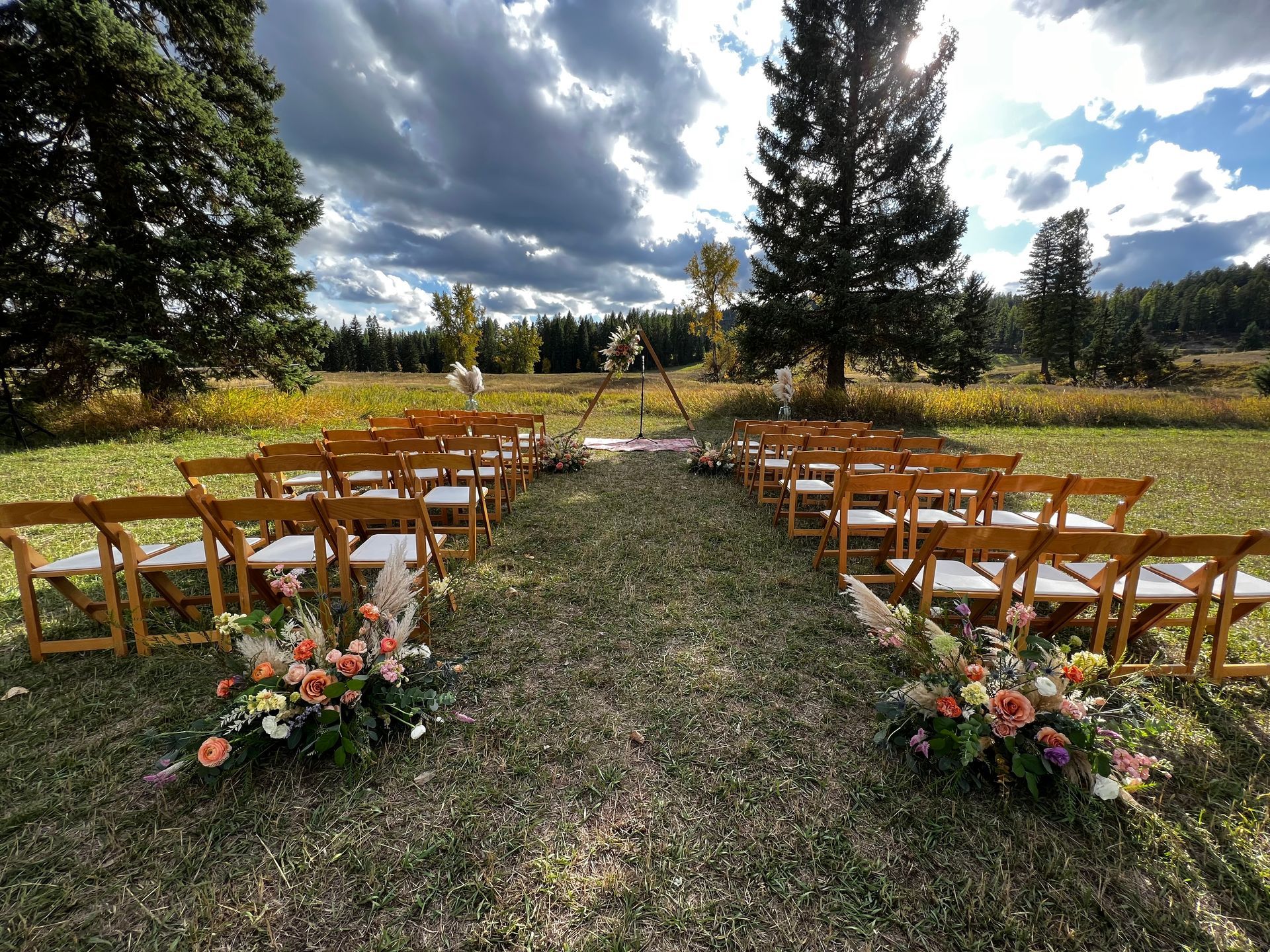 A row of wooden chairs are lined up in a field for a wedding ceremony.