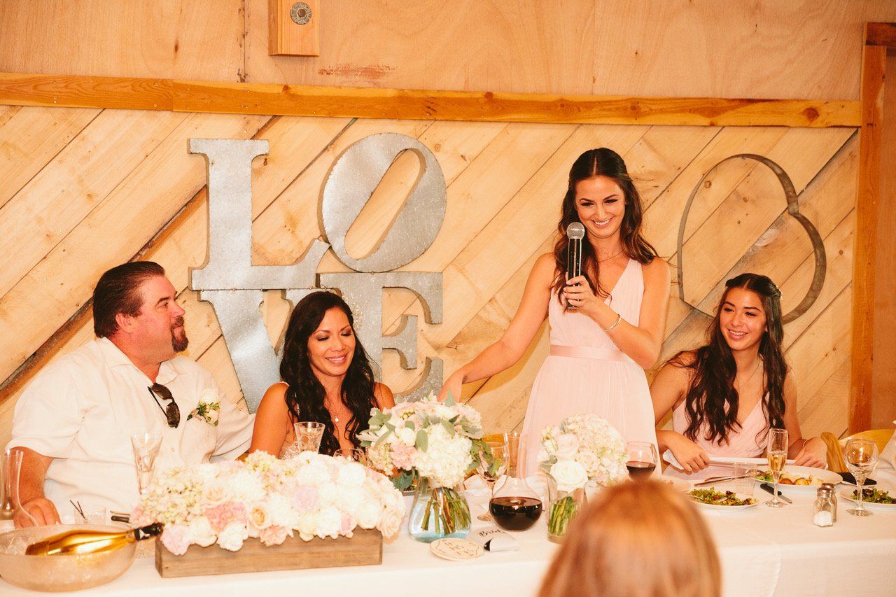 A woman is giving a speech at a wedding reception while holding a microphone.