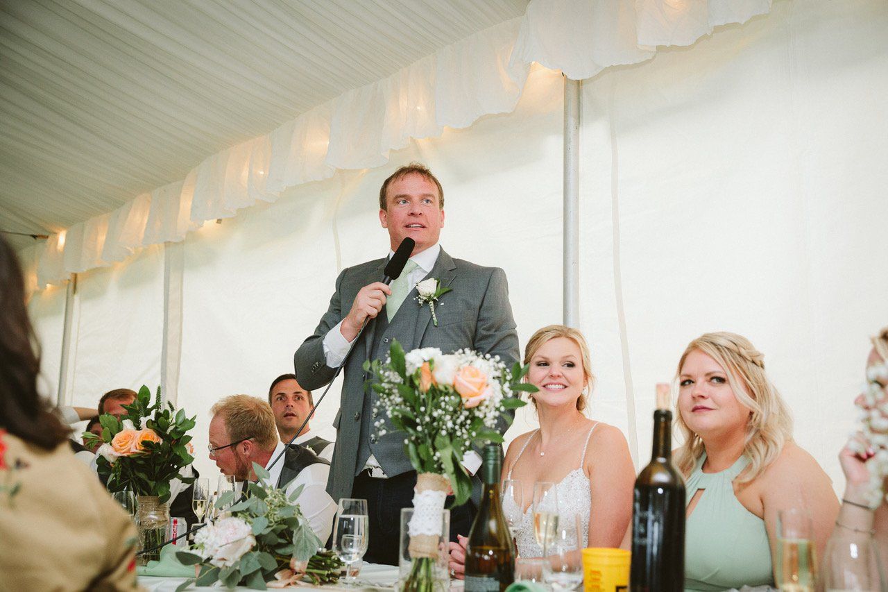 A man is giving a speech at a wedding reception in a tent.