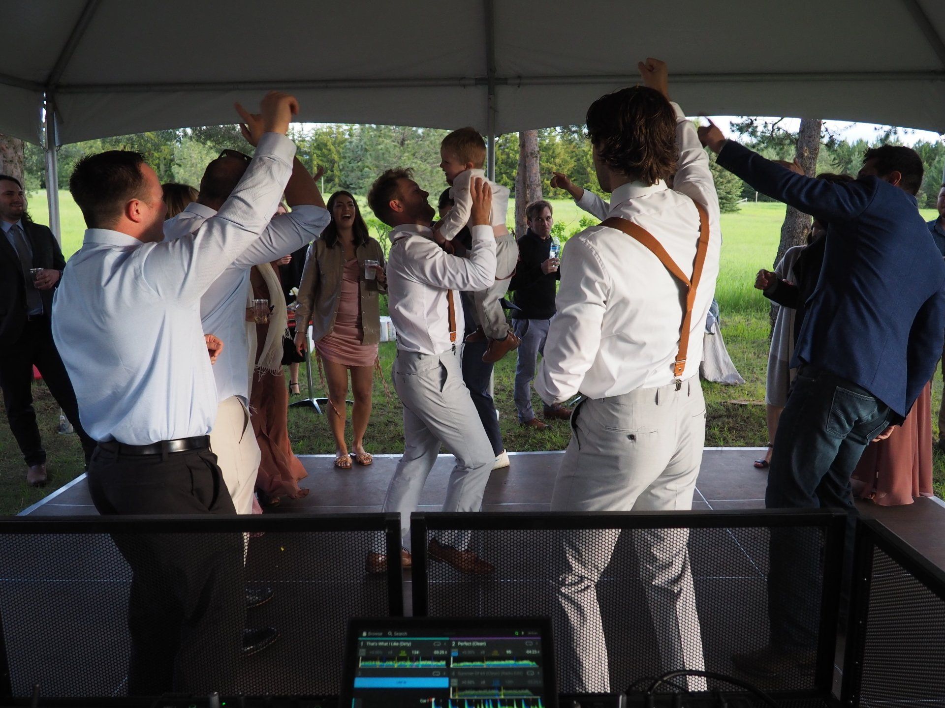 A group of men are dancing on a stage under a tent.