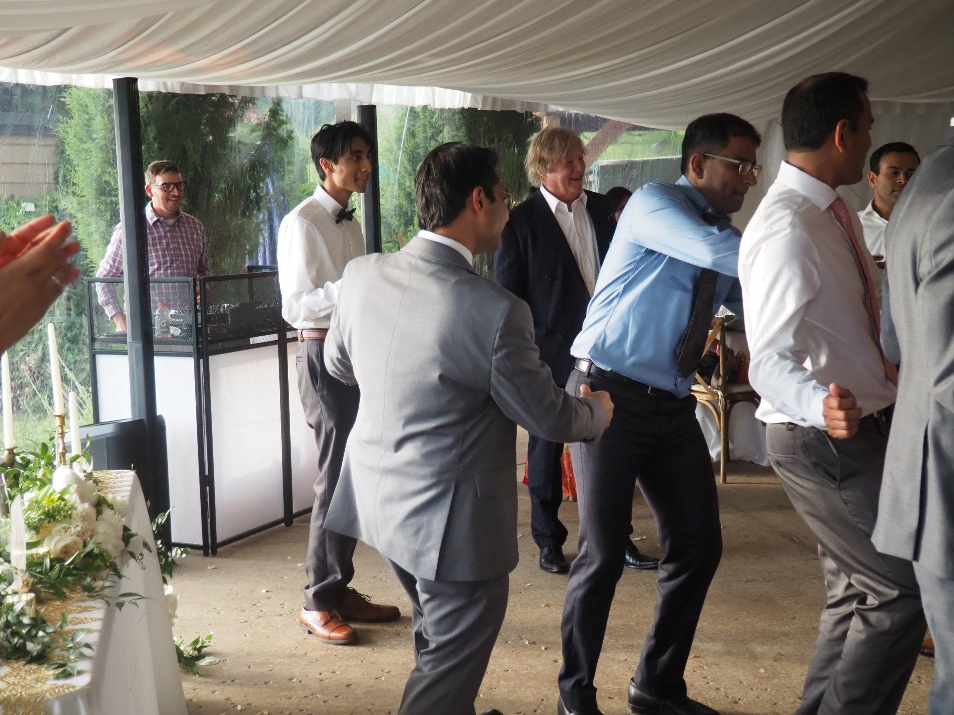A group of men are dancing under a tent at a wedding reception.