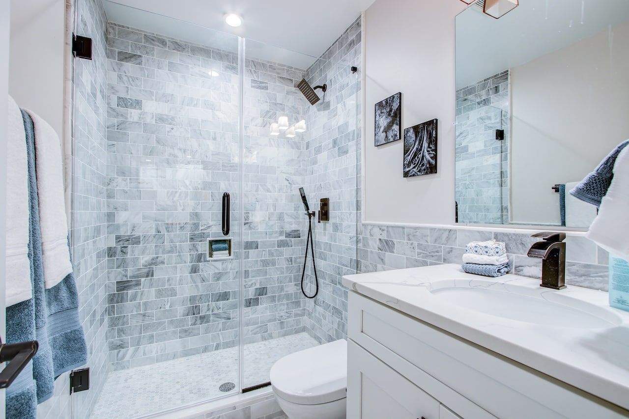 AD Construction NJ - Modern bathroom with marble tile shower, white vanity, and toilet; black fixtures.