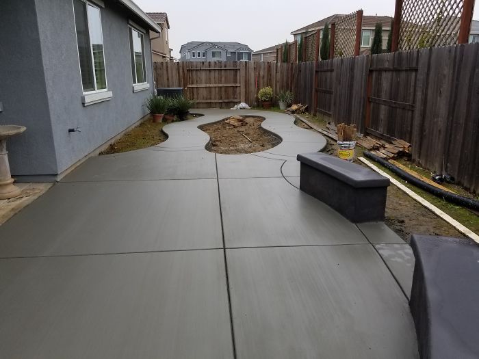 AD Construction NJ - Newly poured gray concrete patio with curved pathway, small garden, and wooden fence.