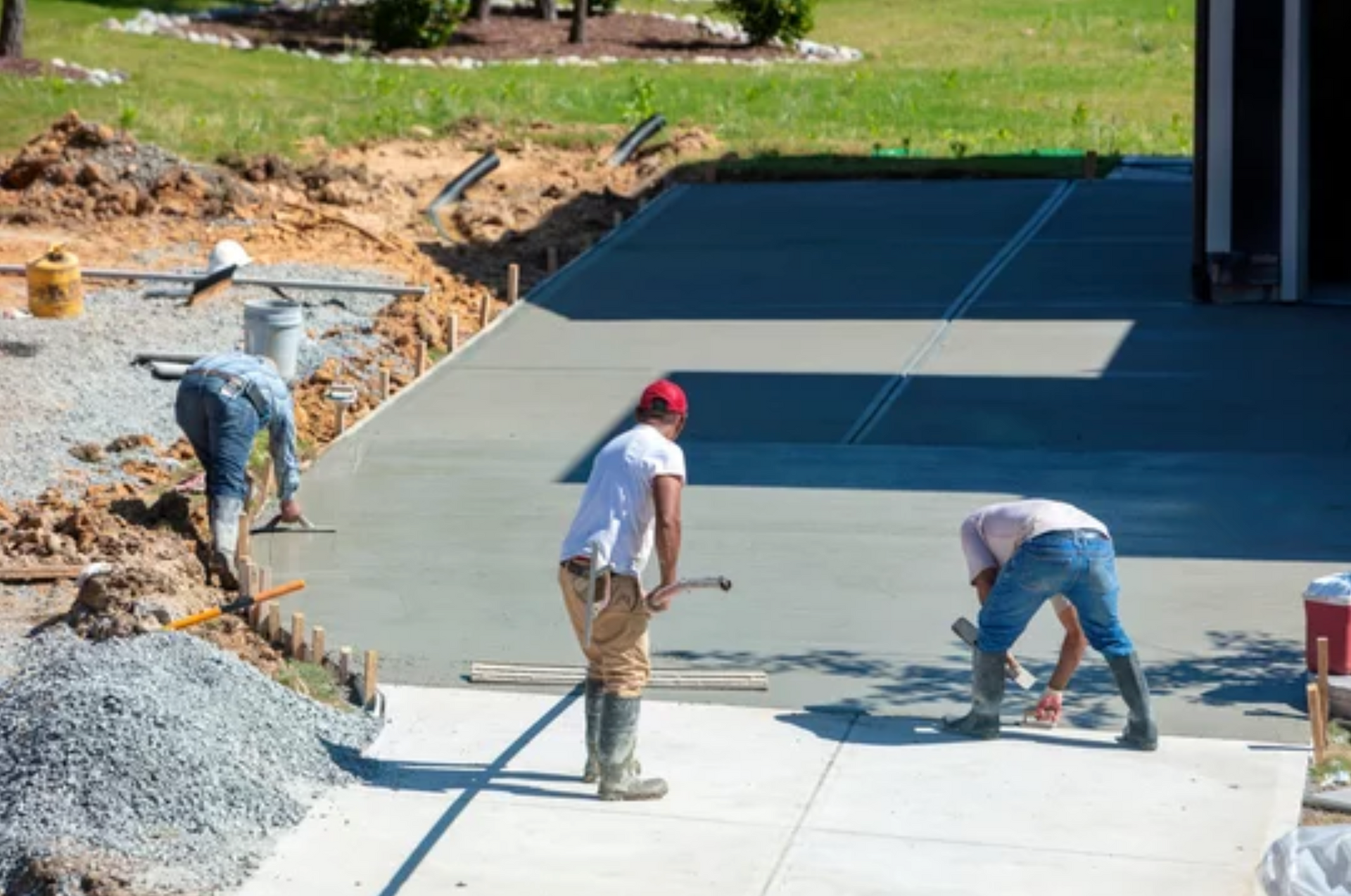 AD Construction NJ - Three construction workers smoothing wet concrete driveway with tools.