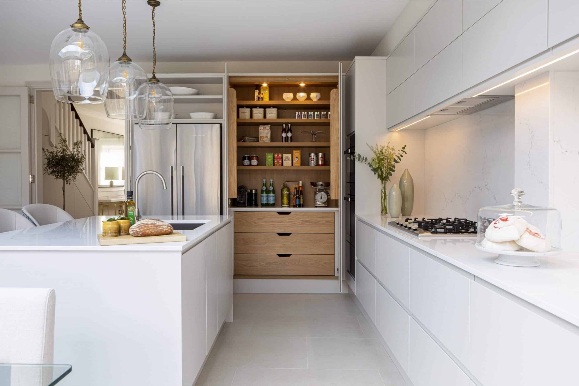 AD Construction NJ - Modern white kitchen with island, pantry, stainless steel refrigerator, and hanging glass pendant lights