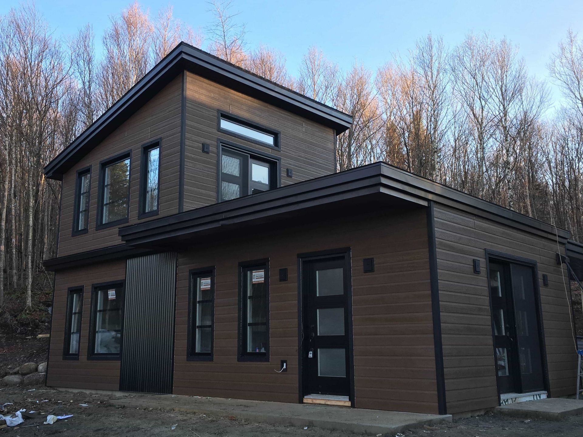 AD Construction NJ - Two-story modern brown house with black trim, windows, and door, surrounded by trees.