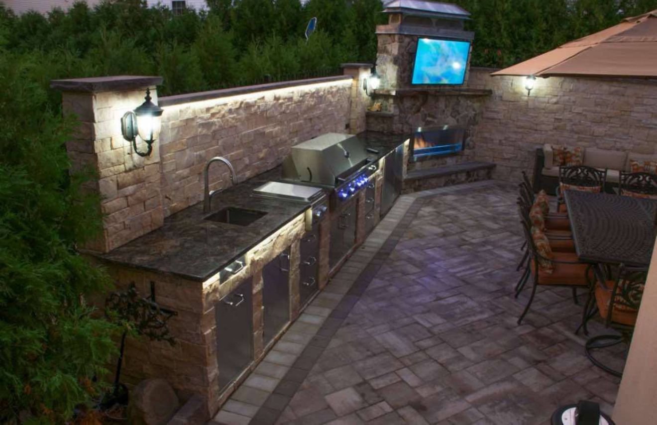 AD Construction NJ - Outdoor kitchen with grill, sink, and TV on a stone patio with seating.