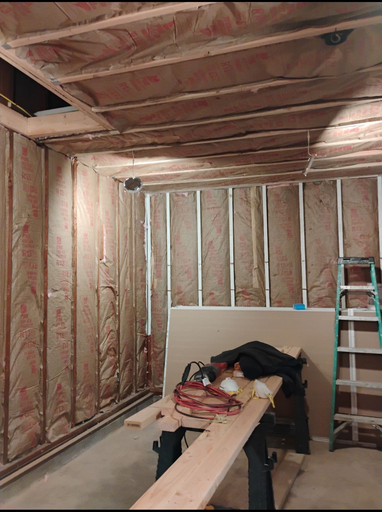 AD Construction NJ - Interior of unfinished room; insulation visible in walls and ceiling; lumber and tools on workbench.