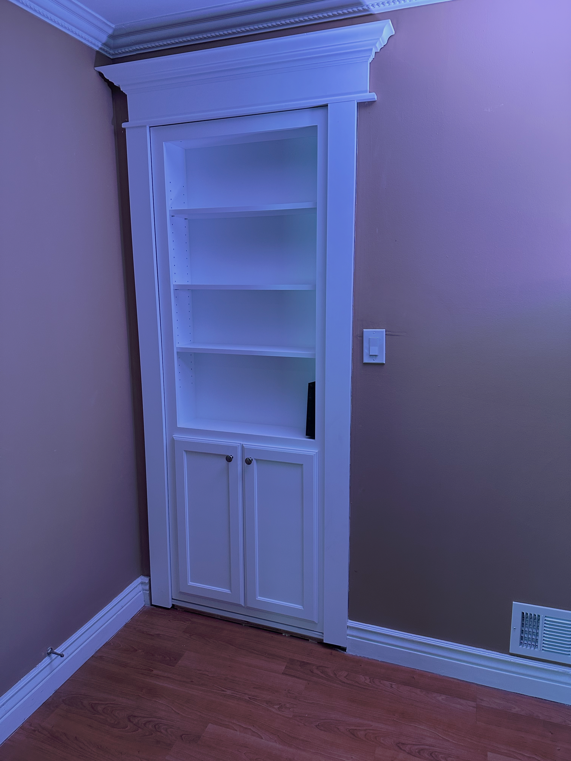 AD Construction NJ - Built-in white cabinet with shelves and doors in a corner of a room, framed by trim.