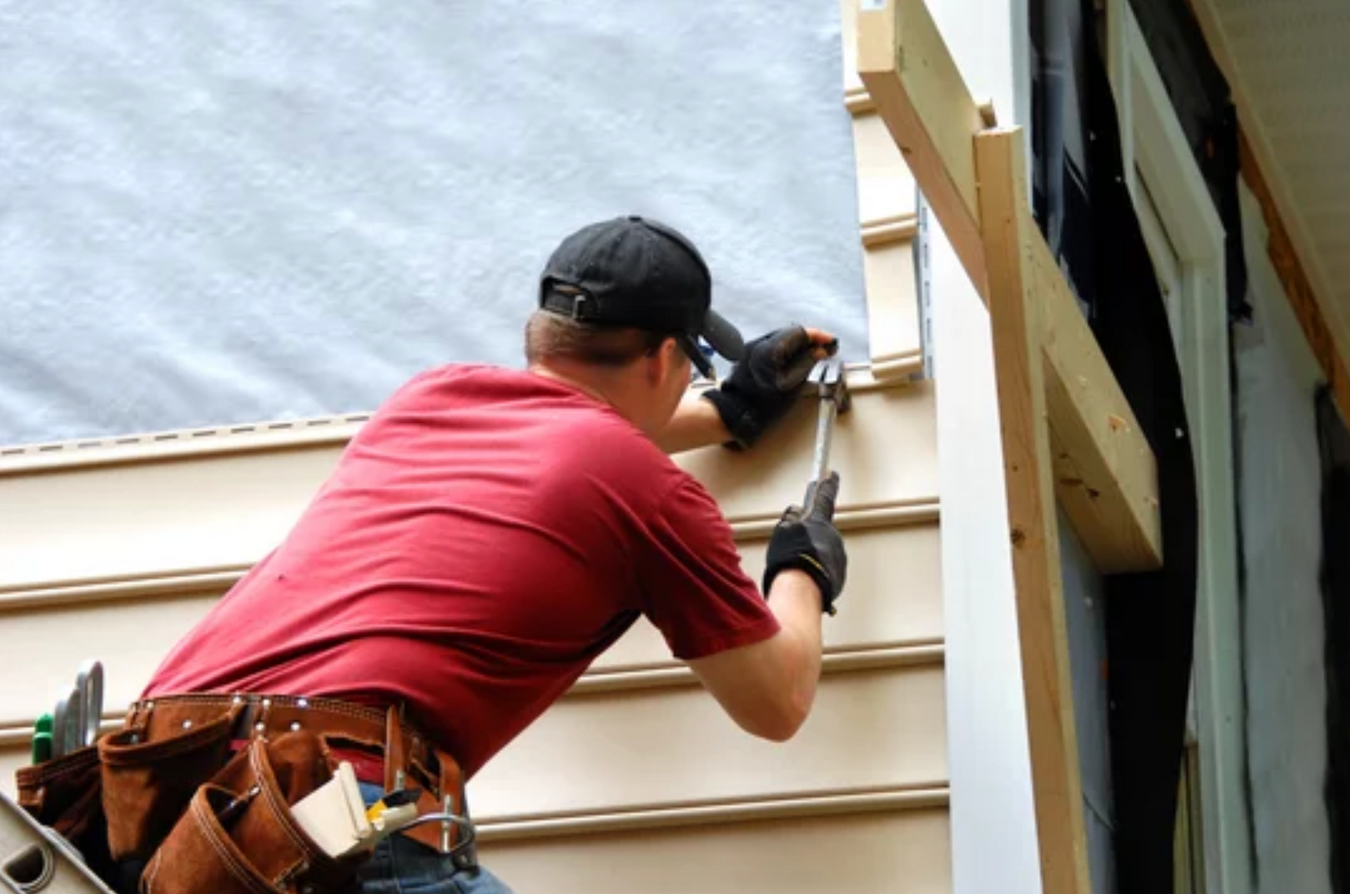 AD Construction NJ - Person in red shirt and cap installing siding on a building, working near a window.