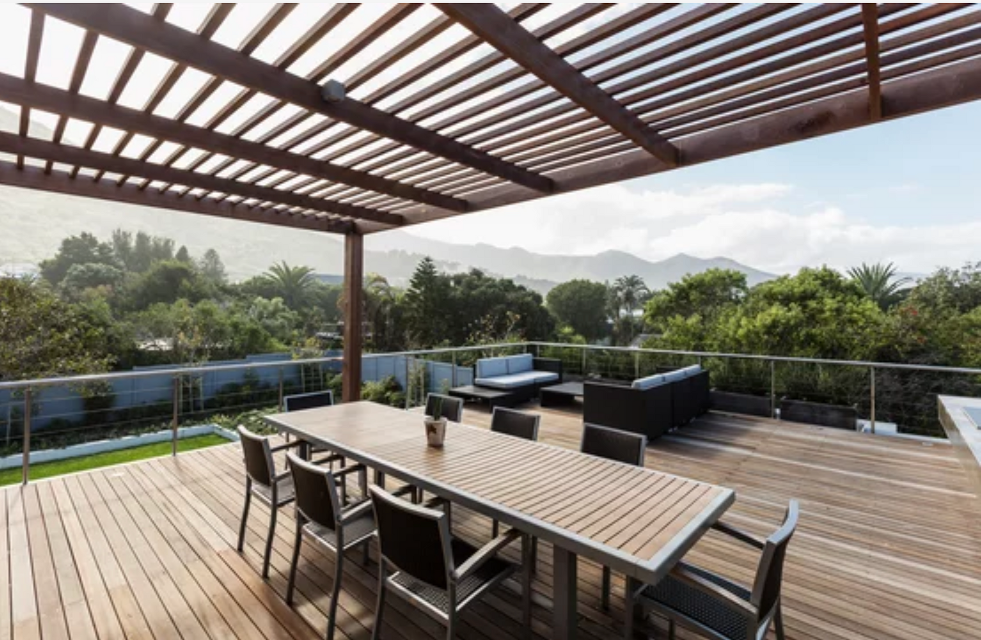 AD Construction NJ - Wooden deck with pergola, table and chairs, outdoor seating area, trees and mountains in background.