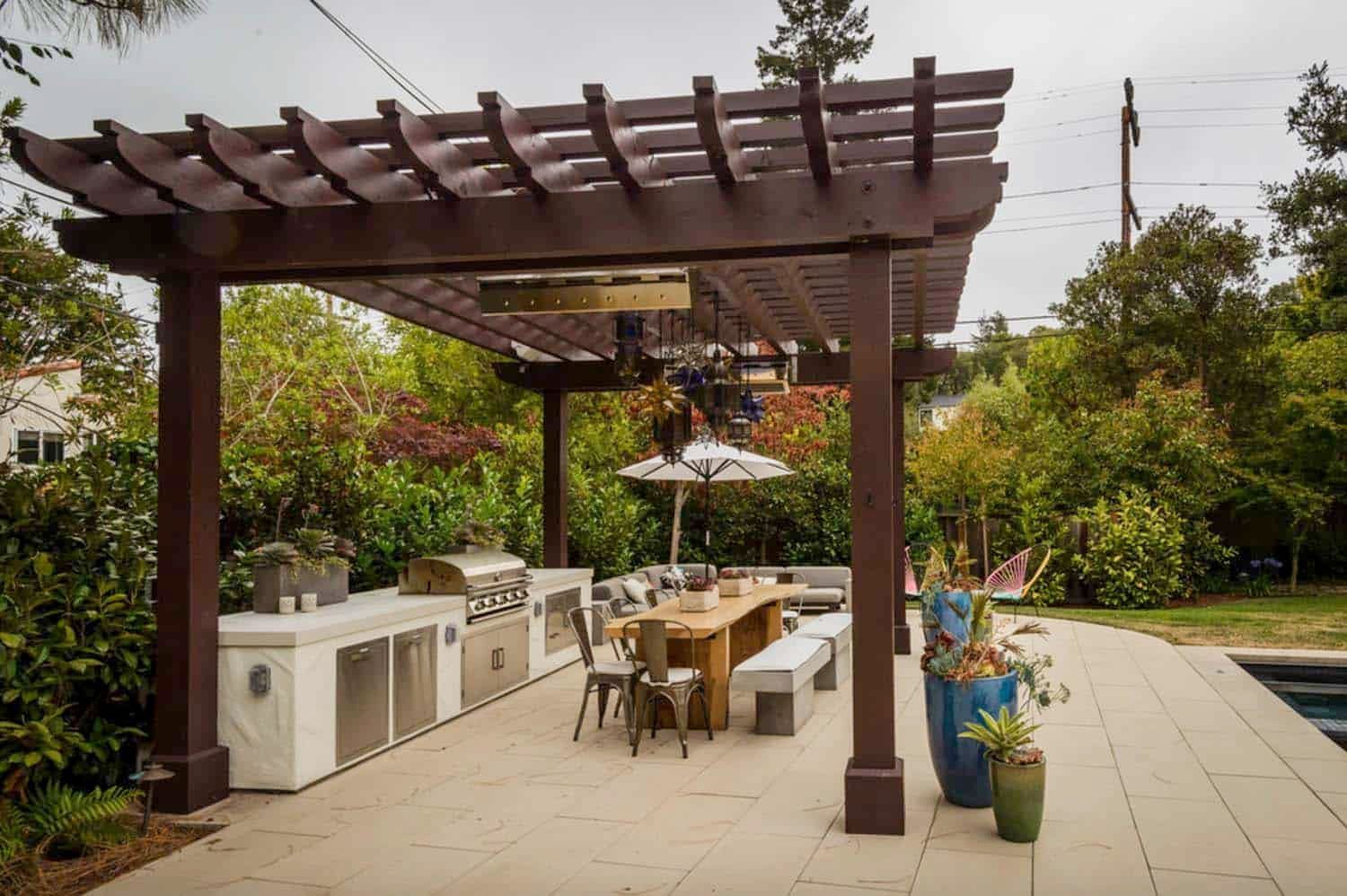 AD Construction NJ - Outdoor kitchen and dining area under a brown pergola. Includes grill, table, benches, and potted plants