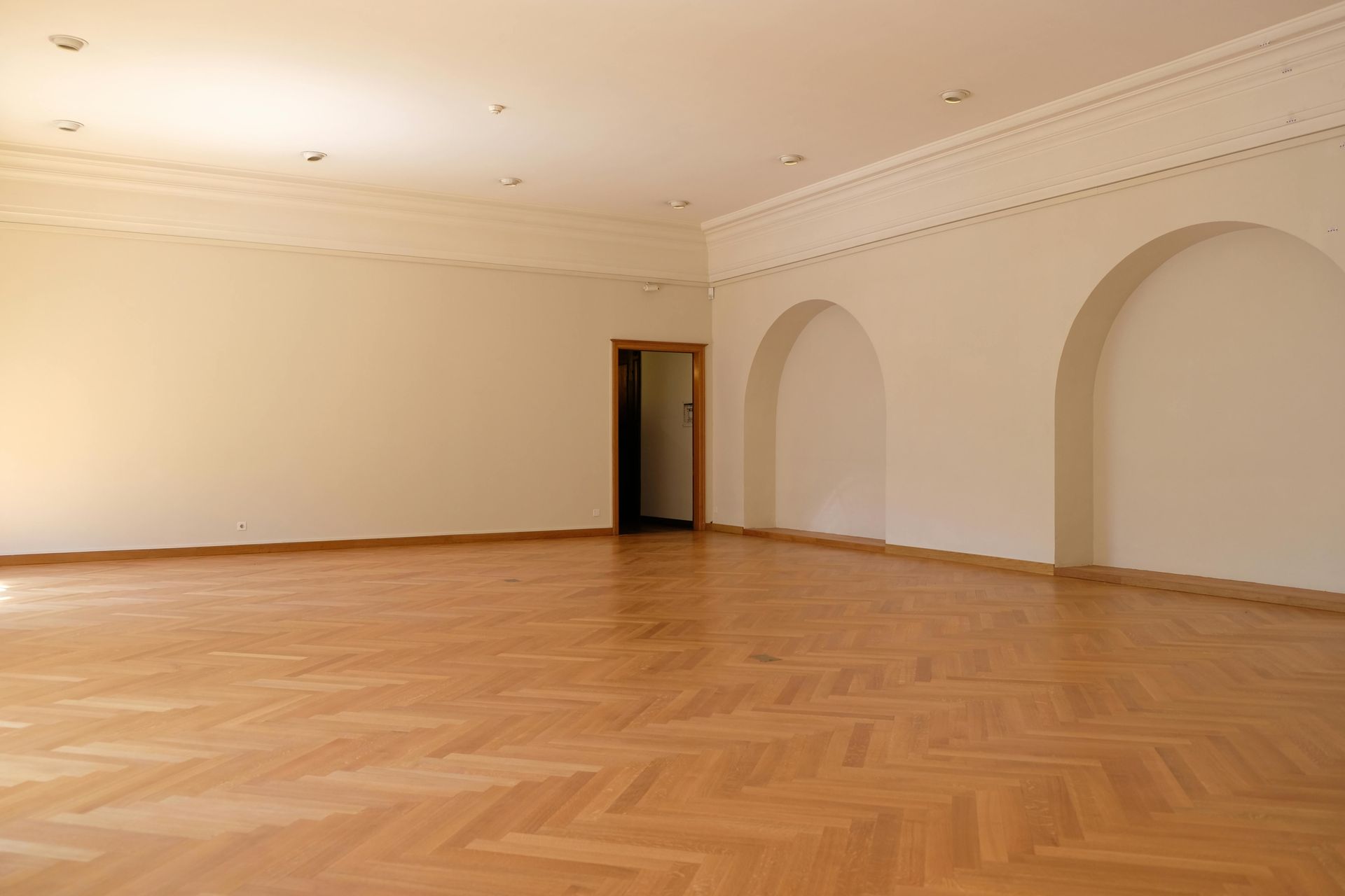 AD Construction NJ - Empty room with light wood parquet flooring, beige walls, and decorative ceiling molding.