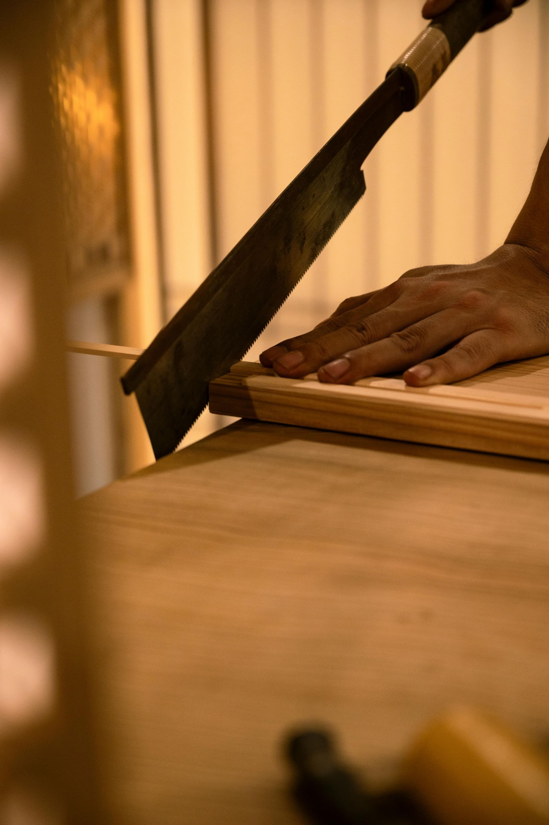 AD Construction NJ - Person using a hand saw to cut a wooden board on a table.