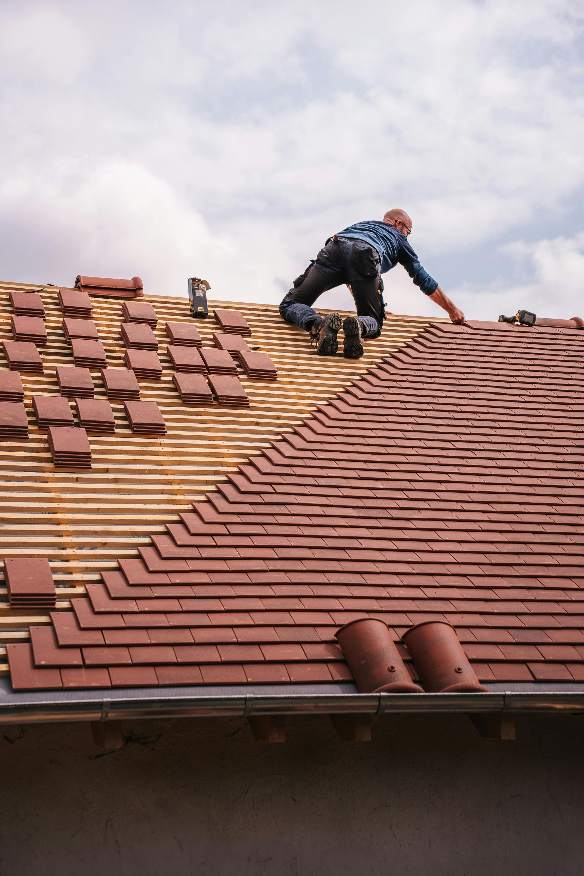 AD Construction NJ - Roofer installing red clay tiles on a rooftop with clear blue sky in background.