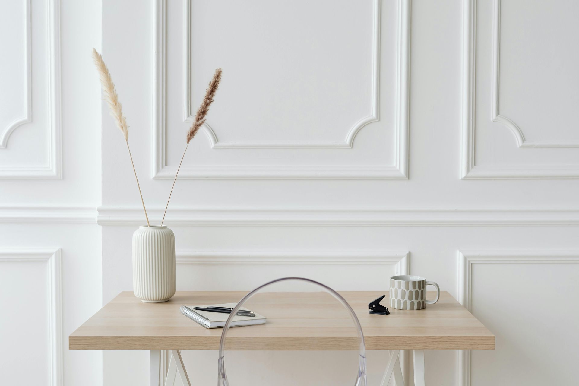 AD Construction NJ - Wooden desk with a vase of dried flowers, a mug, and a tablet in front of a white paneled wall.