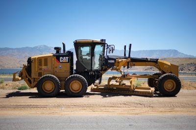 A cat grader is parked on the side of the road.