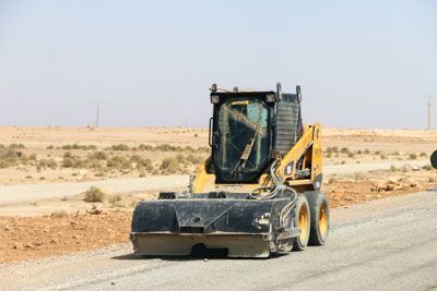 A bulldozer is driving down a dirt road in the desert.