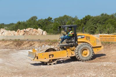 A man is driving a yellow tractor on a dirt road.