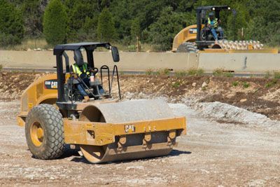 A couple of construction vehicles are driving on a dirt road.