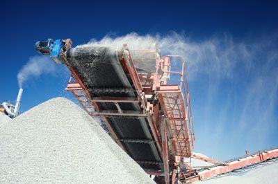 A conveyor belt is carrying a pile of gravel and smoke is coming out of it.