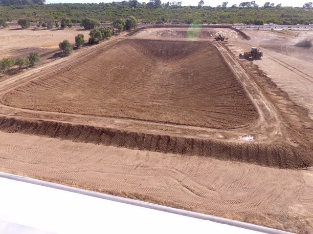 An aerial view of a large dirt field with trees in the background.