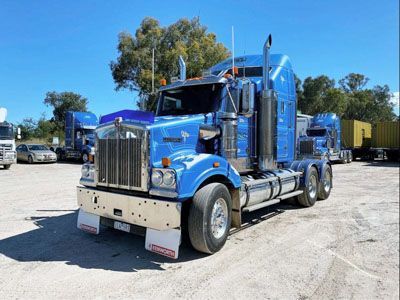 A blue semi truck is parked in a dirt lot.