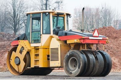 A yellow and red road roller is parked on the side of the road.