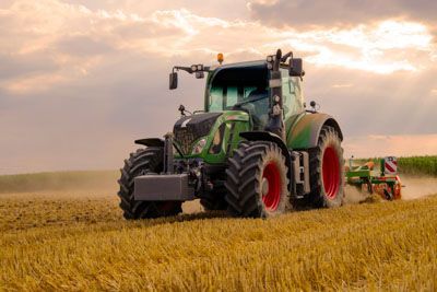 A green tractor is plowing a field of wheat.