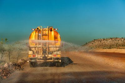 A yellow truck is spraying water on a dirt road.