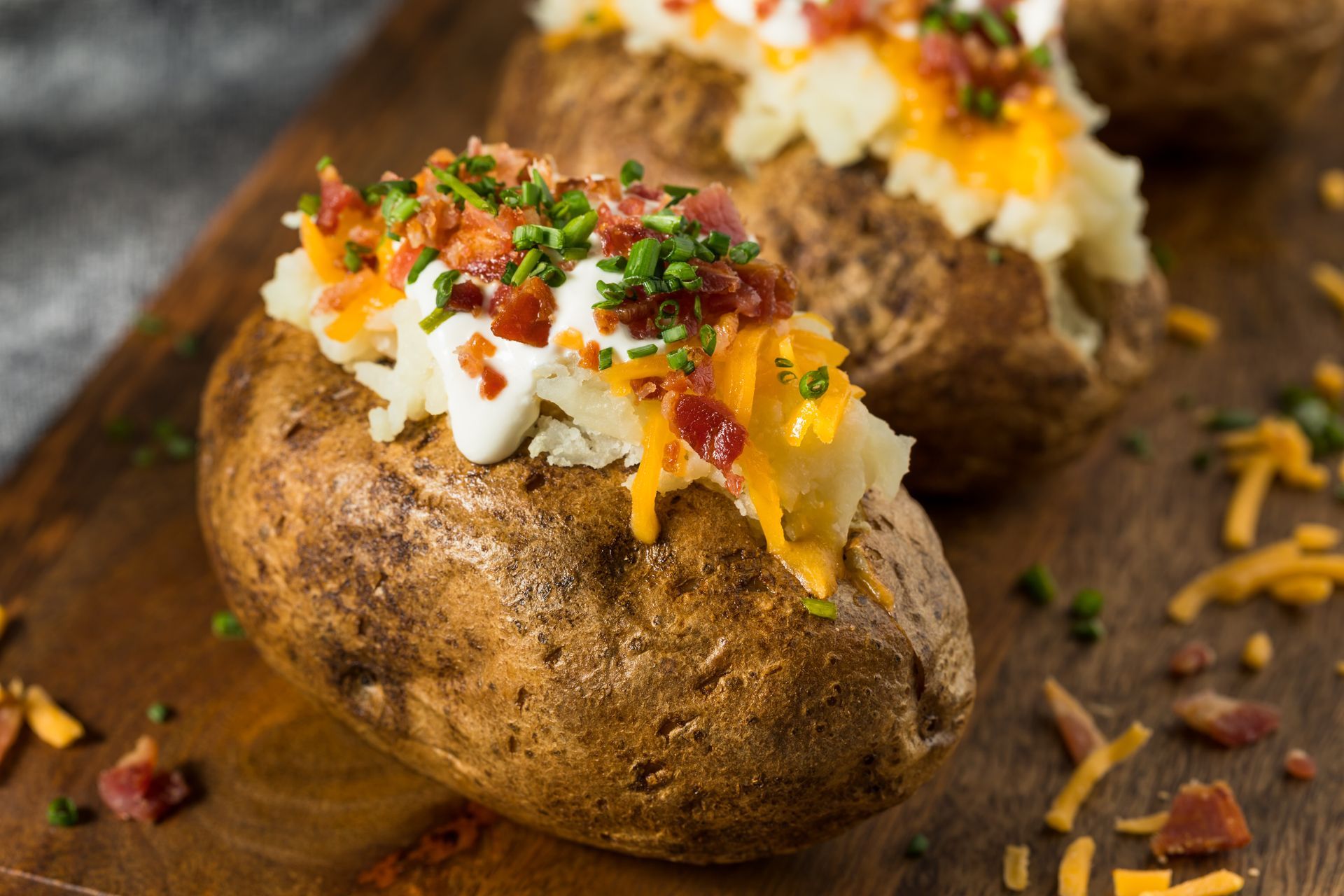 Baked potatoes topped with cheese, bacon, sour cream, and chives on a wooden board.