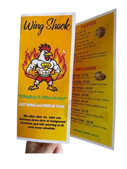 Person holding a dark restaurant menu, looking at the food options, seated at a table.