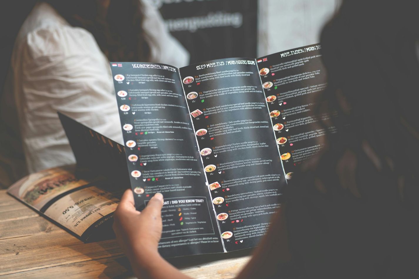 Person holding a dark restaurant menu, looking at the food options, seated at a table.